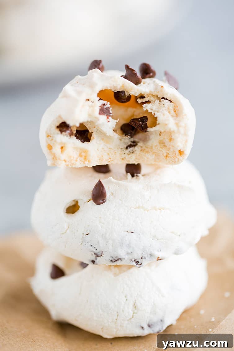 A stack of golden-brown chocolate chip meringue cookies, one with a bite taken out, showcasing its airy interior.