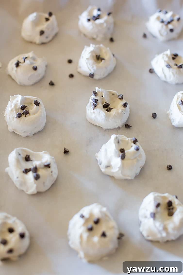 A baking sheet filled with unbaked chocolate chip meringue cookie dollops, perfectly shaped and ready for the oven.