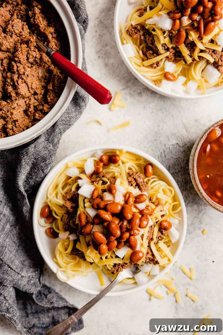 Overhead photo of plates piled high with Cincinnati chili and toppings including shredded cheese, diced onions, and beans, illustrating the '5-way' serving style.