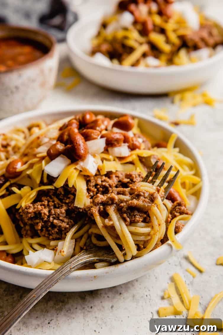 A fork twirling together spaghetti noodles with Cincinnati chili, illustrating the satisfying texture of the dish.