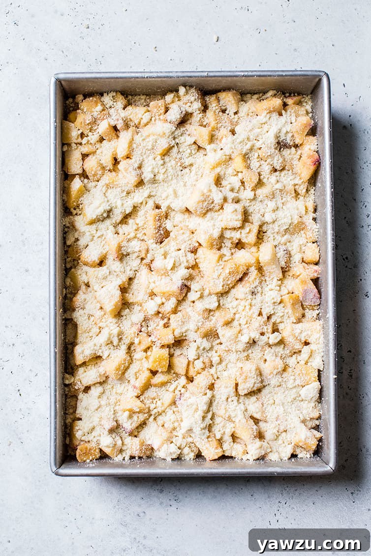 A baking pan filled with unbaked peach crumb bars, topped with a generous layer of crumble.