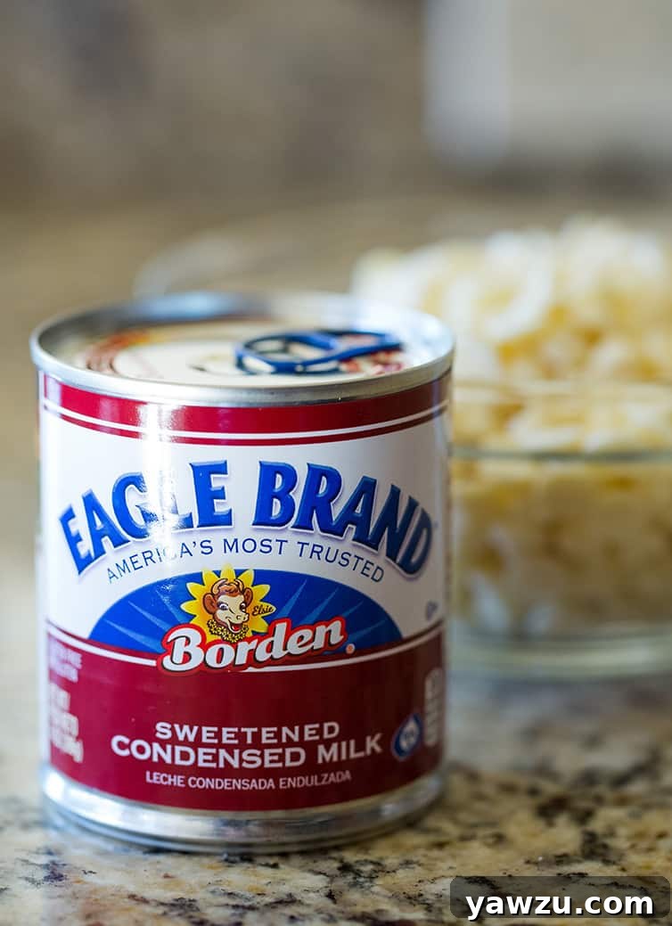 A can of Eagle Brand sweetened condensed milk sits beside a bowl of white chocolate chips on a kitchen counter, ready for baking.