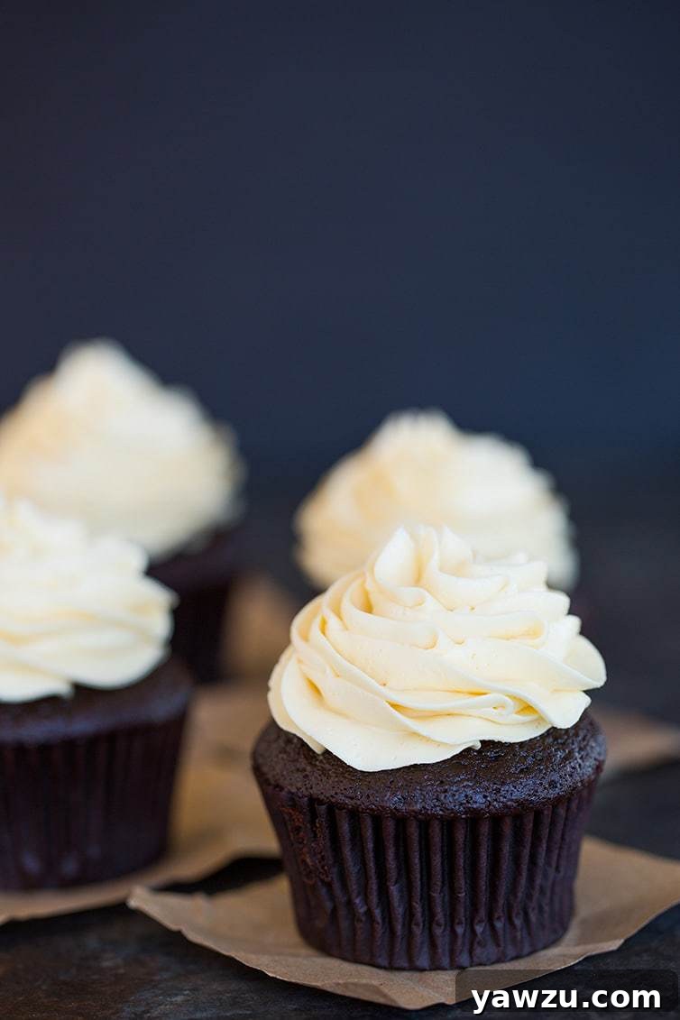 Four perfectly frosted chocolate cupcakes with smooth vanilla buttercream on decorative squares, ready to be enjoyed.