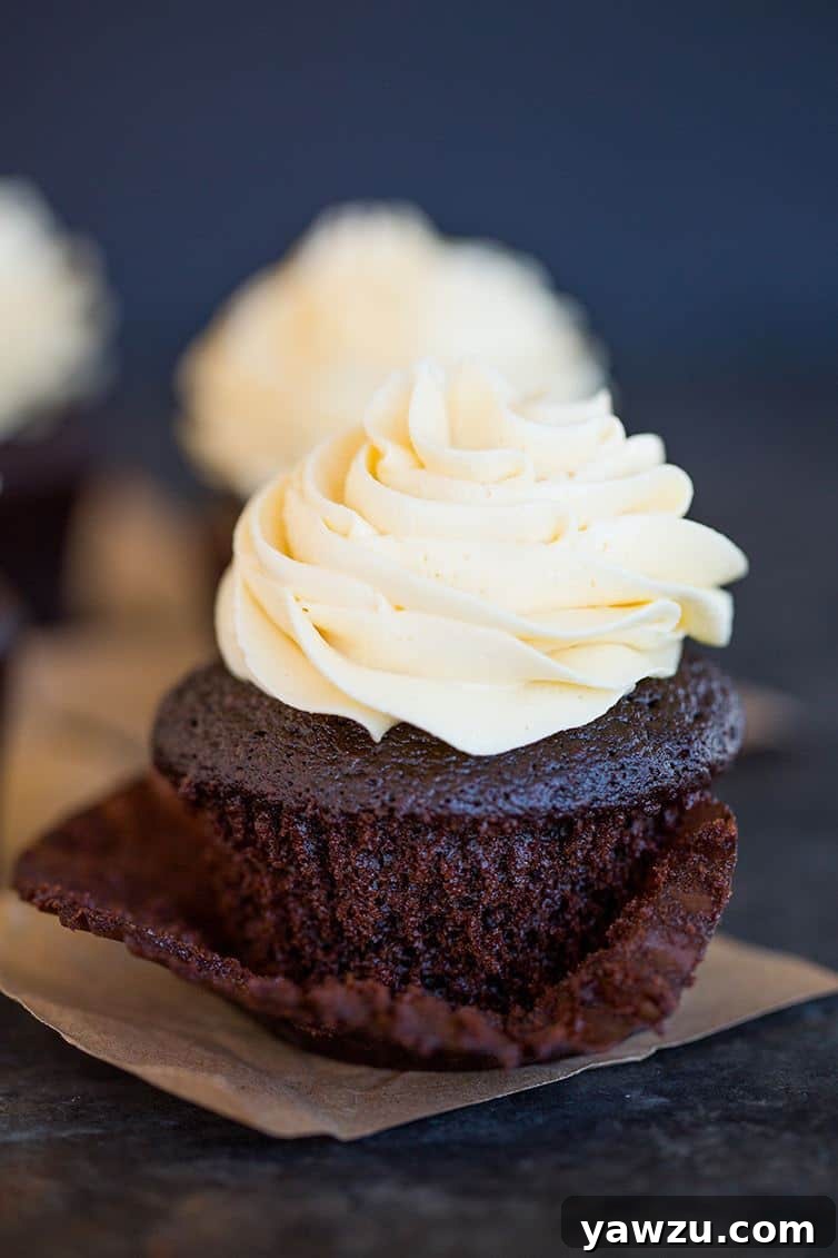 A close-up of a decadent chocolate cupcake with vanilla frosting, its wrapper peeled back to reveal the moist crumb.