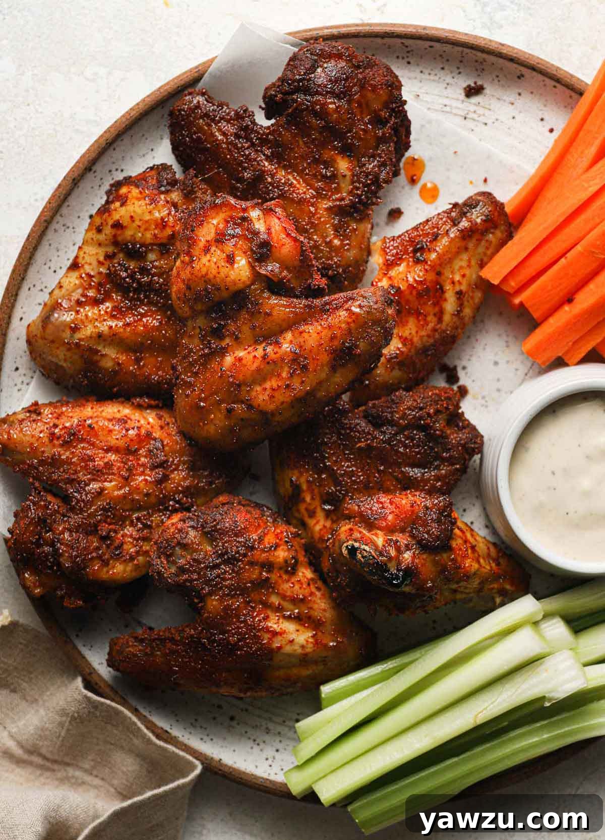A vibrant platter of crispy baked chicken wings alongside a bowl of ranch dressing and crisp carrot and celery sticks.
