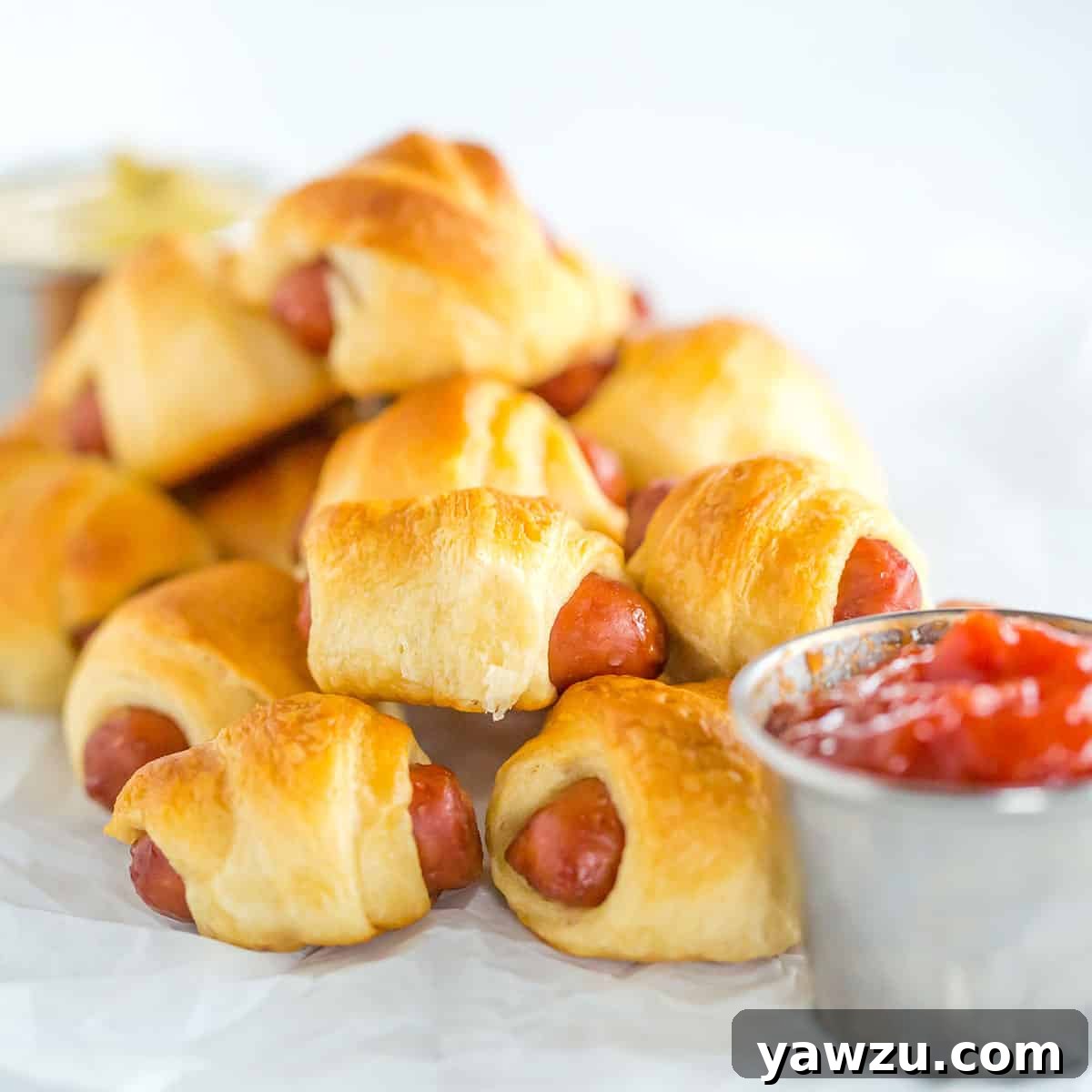 Mini hot dogs wrapped in crescent rolls on parchment paper, ready to bake.