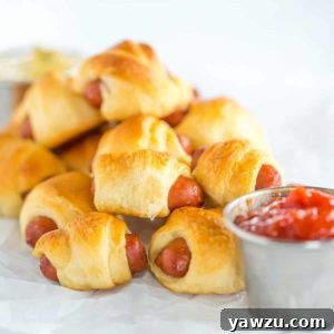 Mini hot dogs wrapped in crescent rolls on parchment paper.
