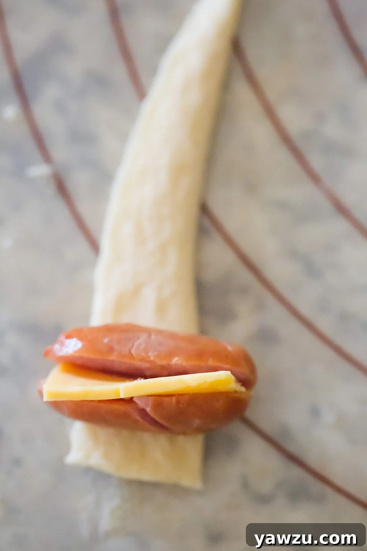 Mini hot dog with cheese stuffed inside, sitting on a strip of crescent roll dough, ready to be rolled.