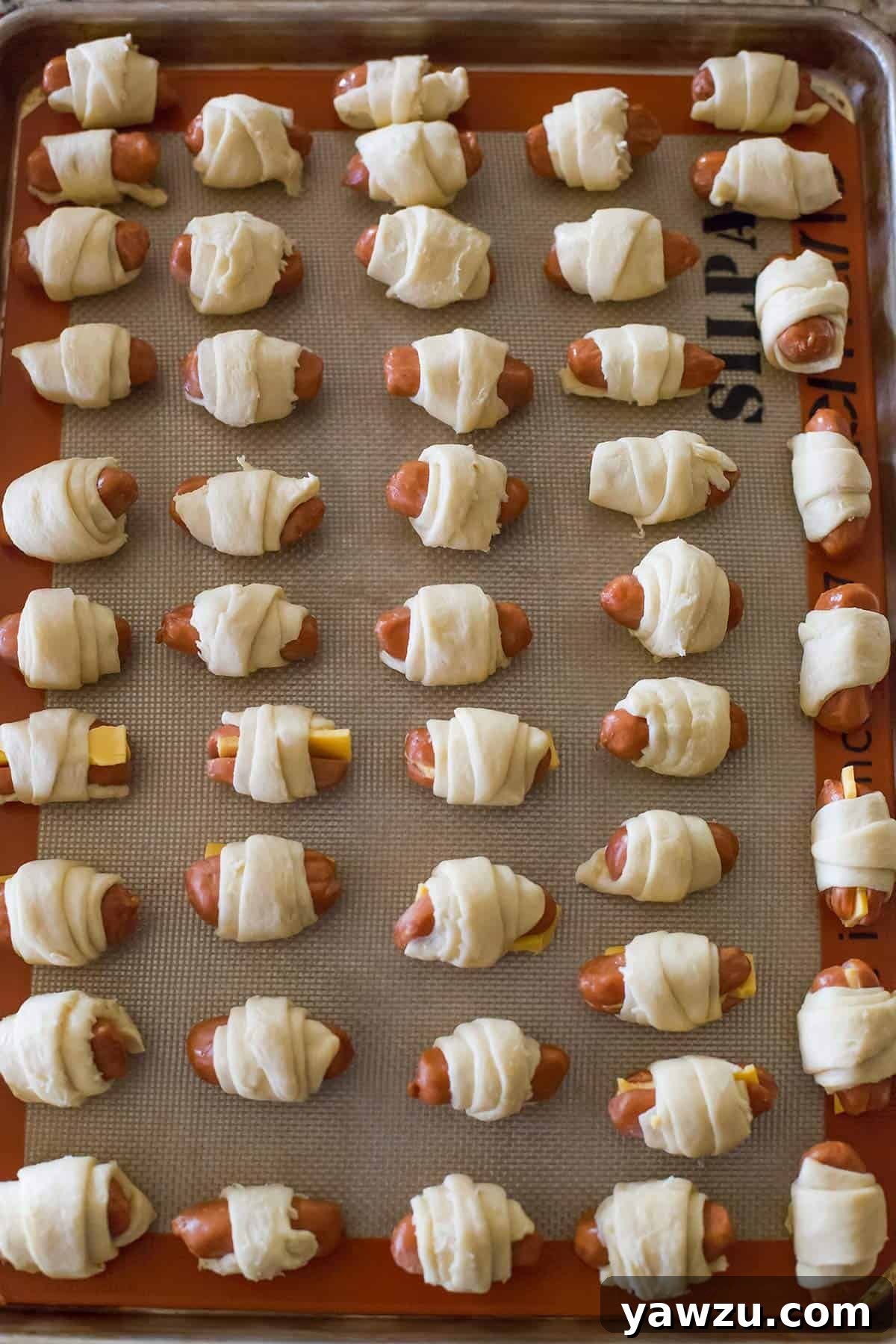 Assembled pigs in a blanket neatly arranged on a baking sheet, ready for the oven.