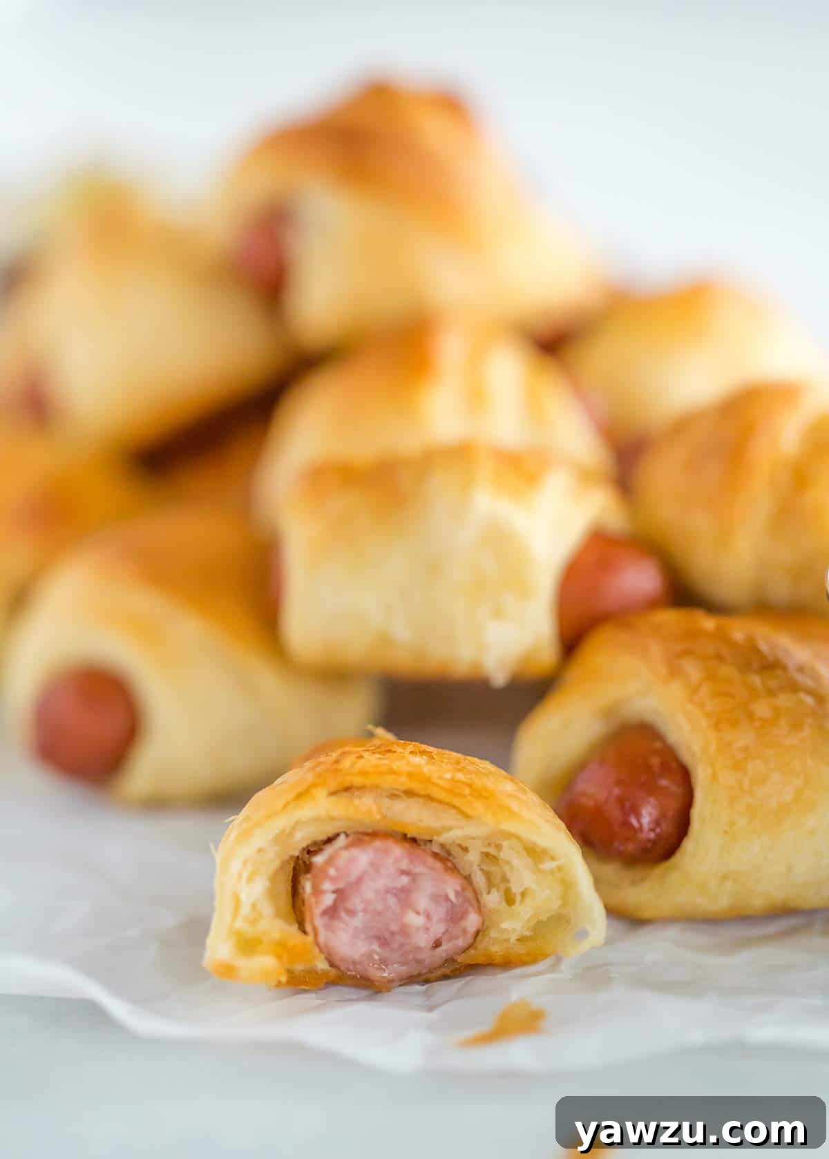A stack of golden-brown pigs in a blanket with one partially bitten, showcasing the juicy interior.