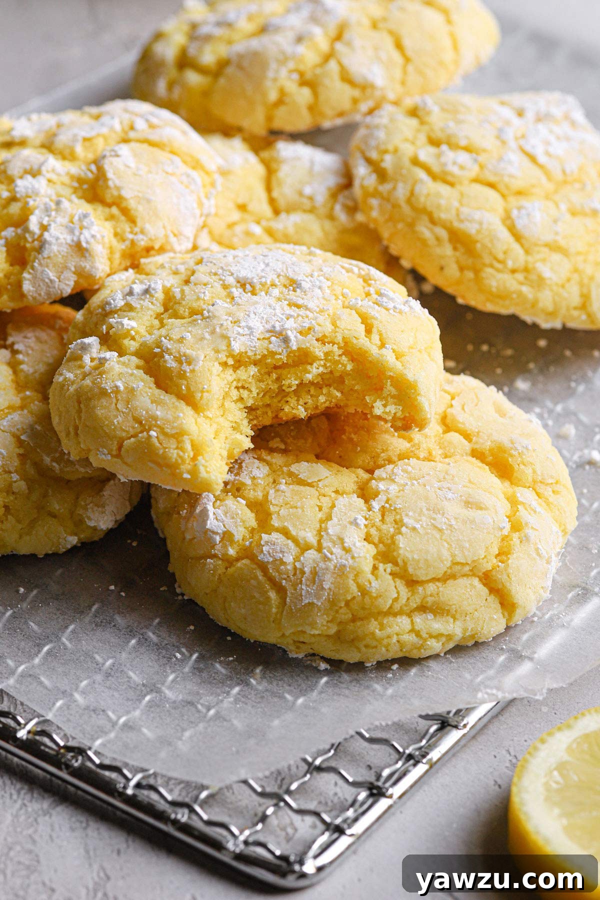 A few lemon crinkle cookies resting on a wire cooling rack, with one in the foreground showing a bite taken out.