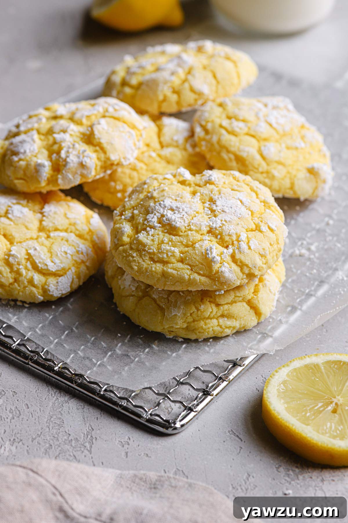 A few lemon crinkle cookies resting on a wire cooling rack with a lemon slice off to the right-hand side.