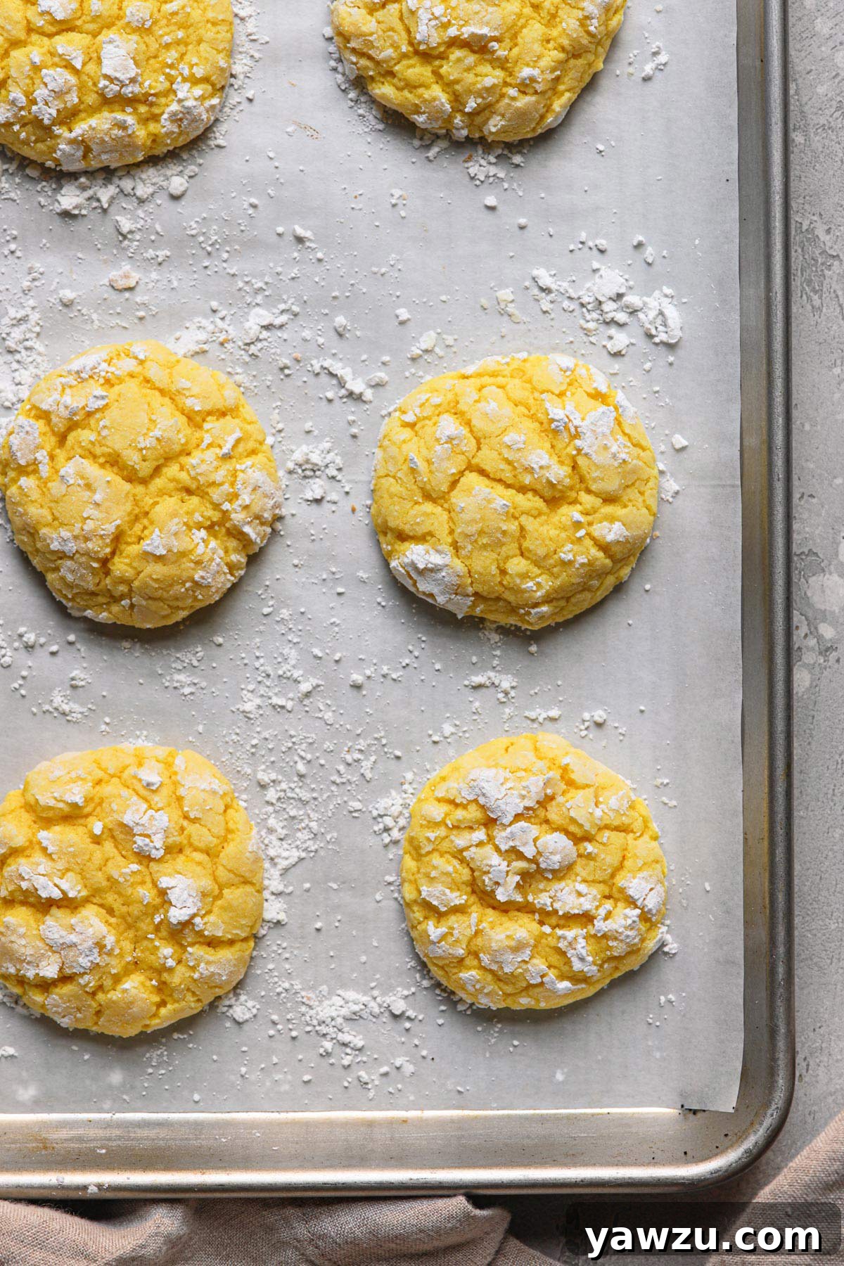 A few lemon crinkle cookies resting on a lined baking sheet dusted in powdered sugar.