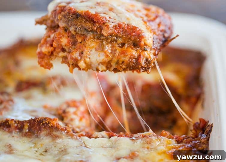 A slice of eggplant parmesan being lifted out of the pan, showcasing layers of eggplant, sauce, and cheese.