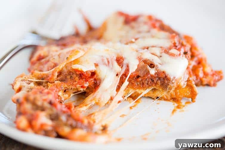 A perfectly cut slice of eggplant parmesan with melted cheese being served, showing distinct layers.