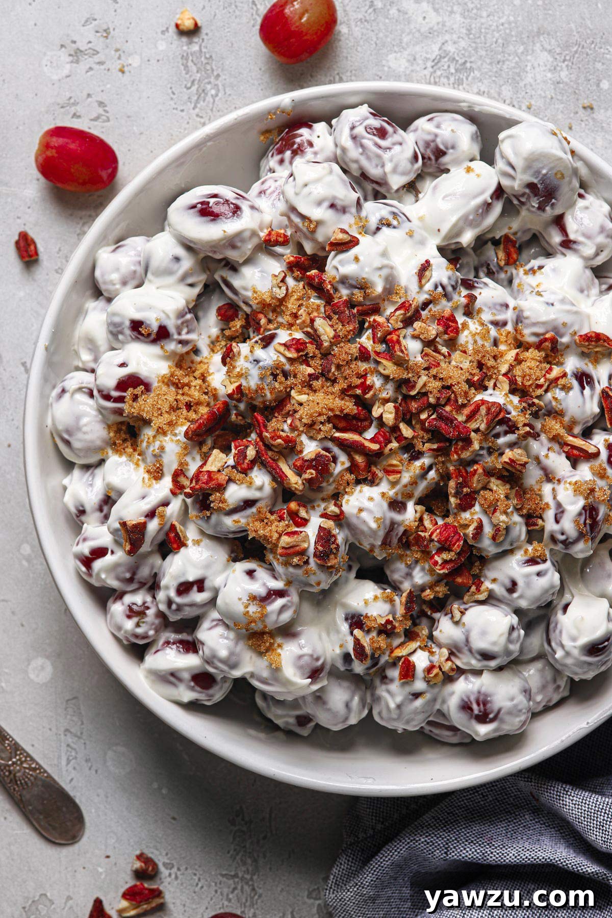 A large white serving bowl filled with homemade grape salad, beautifully topped with golden brown sugar and crunchy chopped toasted pecans, ready to be enjoyed.