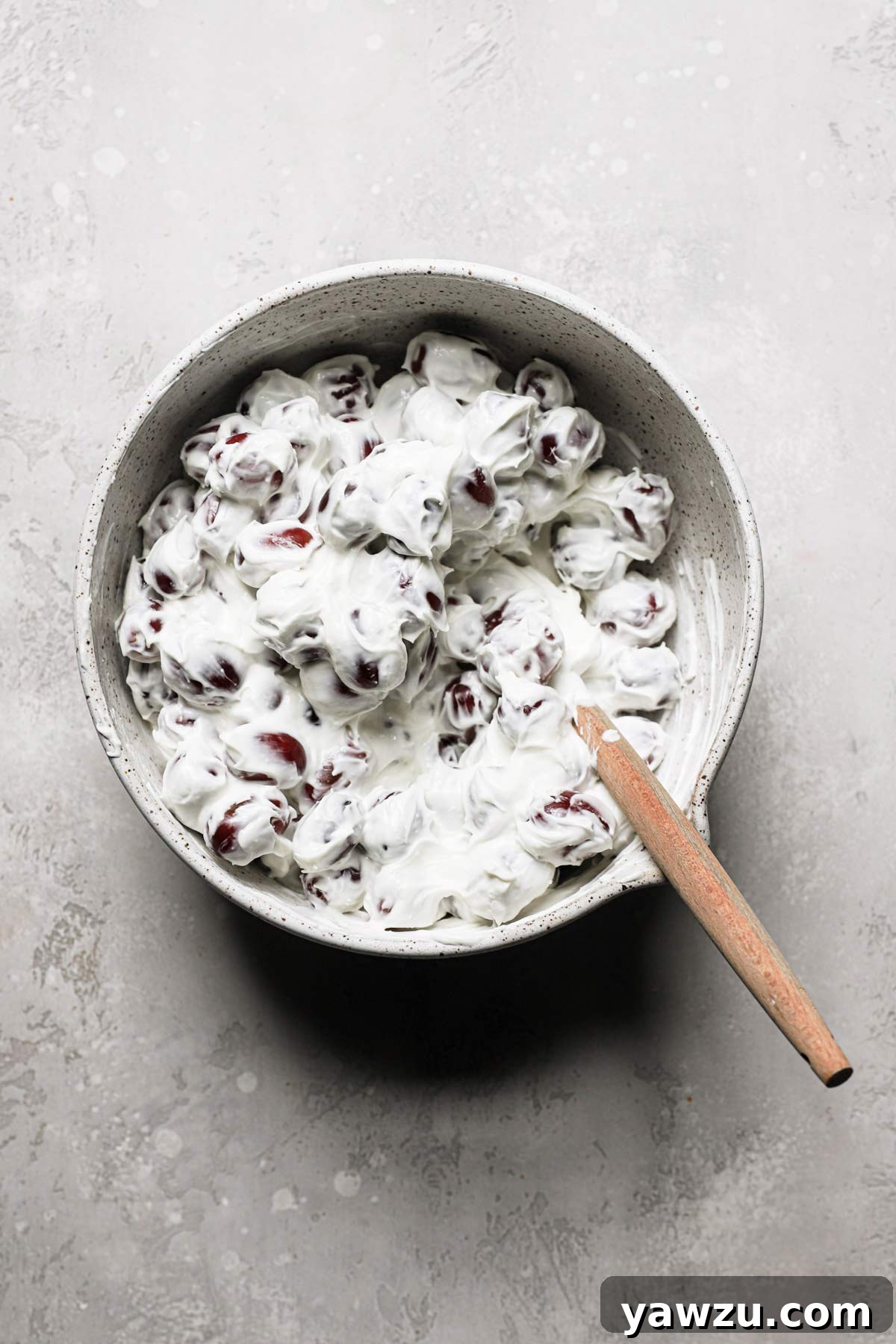 An overhead view of the author gently mixing whole seedless grapes with the homemade cream cheese dressing using a rubber spatula, creating a smooth and even coating for the grape salad recipe.