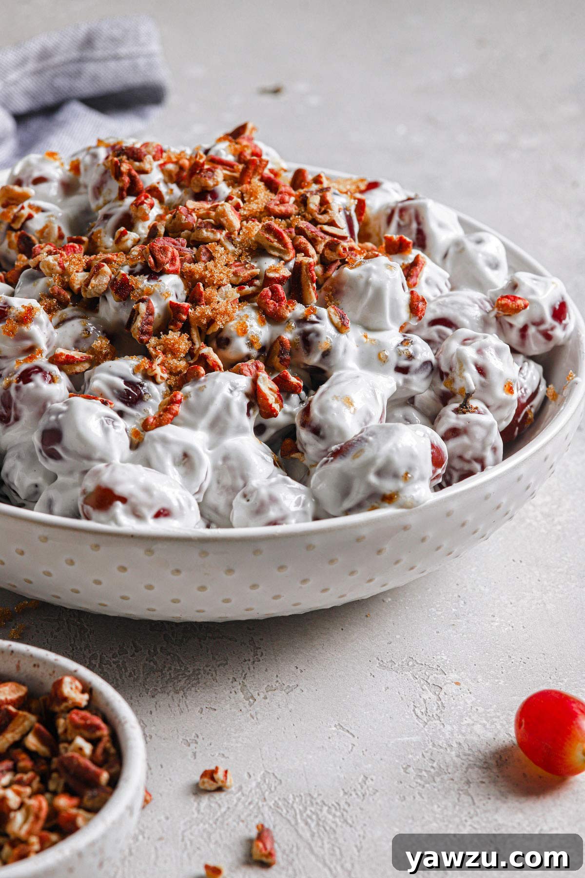 A beautiful side view of a large white serving bowl filled to the brim with this homemade grape salad, elegantly finished with a topping of brown sugar and finely chopped toasted pecans.
