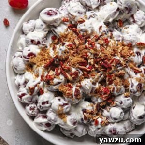 a large white serving bowl filled with this homemade grape salad recipe topped with brown sugar and chopped toasted pecans