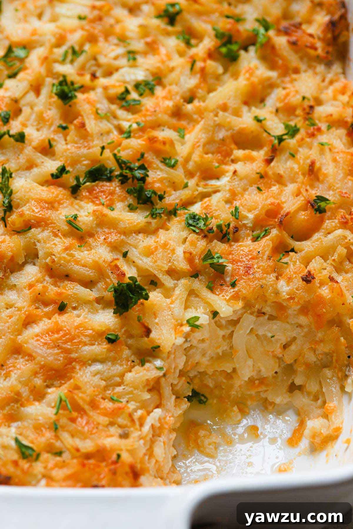 Overhead photo of hashbrown casserole with a large helping taken out of the corner, showcasing its golden-brown top and gooey interior.