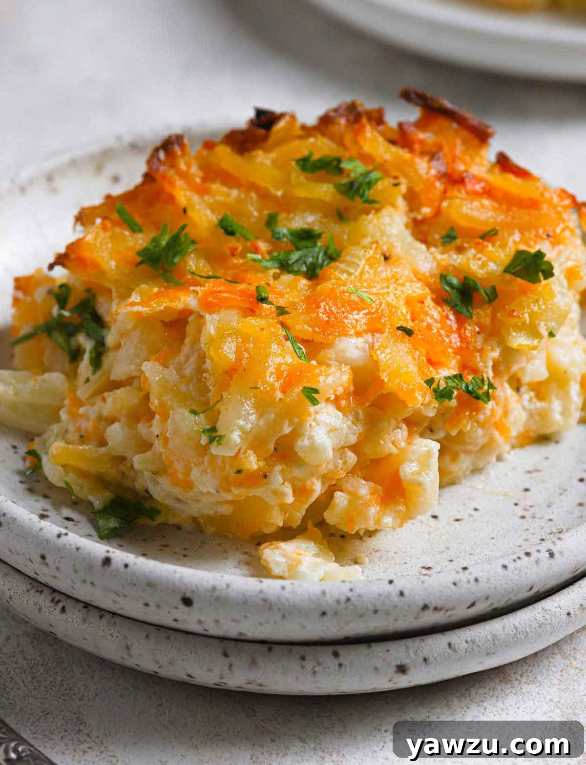 Close up photo of serving of hashbrown casserole on black and white speckled plate, highlighting its cheesy texture.