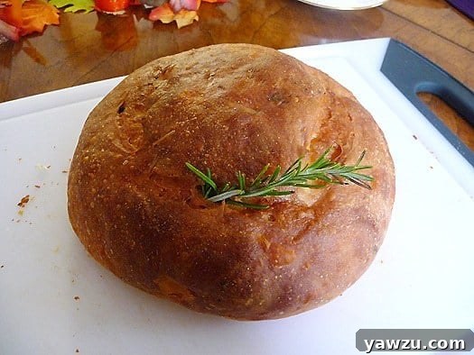 Golden brown loaf of potato rosemary bread with a sprig of fresh rosemary on a wooden cutting board, highlighting its rustic crust.