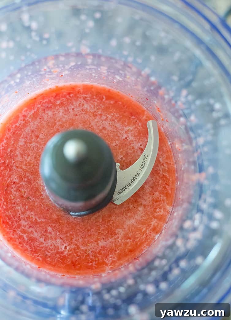 Fresh strawberry puree being prepared in the bowl of a food processor, ready for the topping layer.