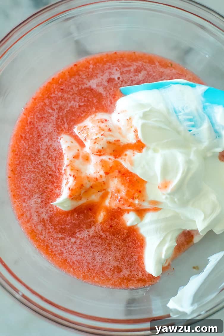 Strawberry puree being mixed with creamy sour cream in a clear glass bowl, showcasing the vibrant pink color.
