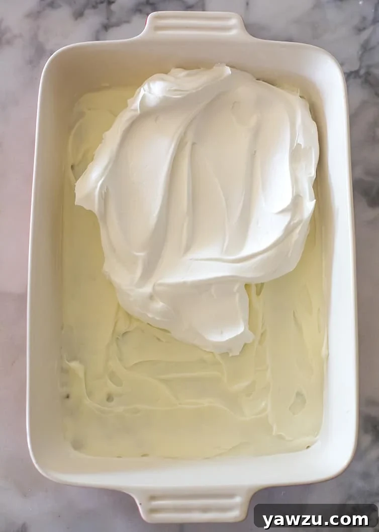 A generous layer of fluffy Cool Whip being spread on top of the cream cheese, creating a soft white layer.