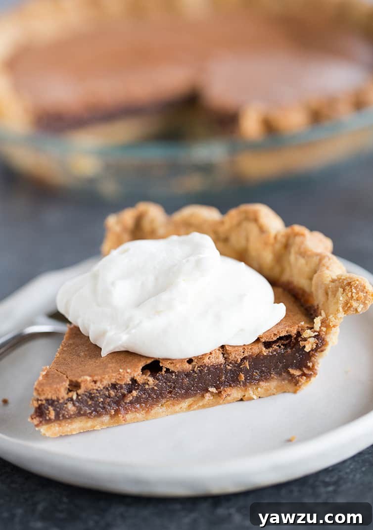 A beautifully sliced chocolate chess pie topped with fresh whipped cream, positioned in front of the remaining pie in its baking dish.