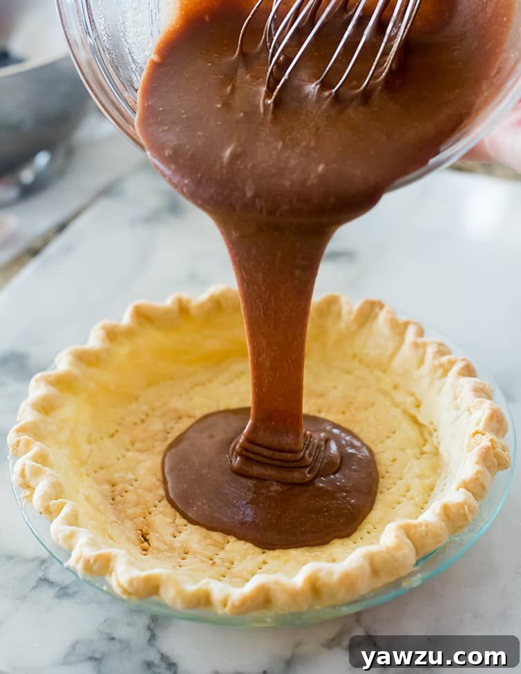The process of pouring rich, dark chocolate batter into a prepared, partially baked pie shell.