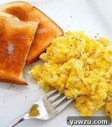 Perfectly cooked scrambled eggs with two pieces of toast on a white plate, ready for a delicious breakfast.