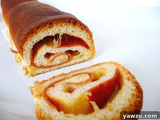 A perfectly sliced loaf of soft cheese and pepperoni bread, revealing a delectable swirl of ingredients, rests invitingly on a white plate. This savory artisan bread promises a delightful culinary experience.