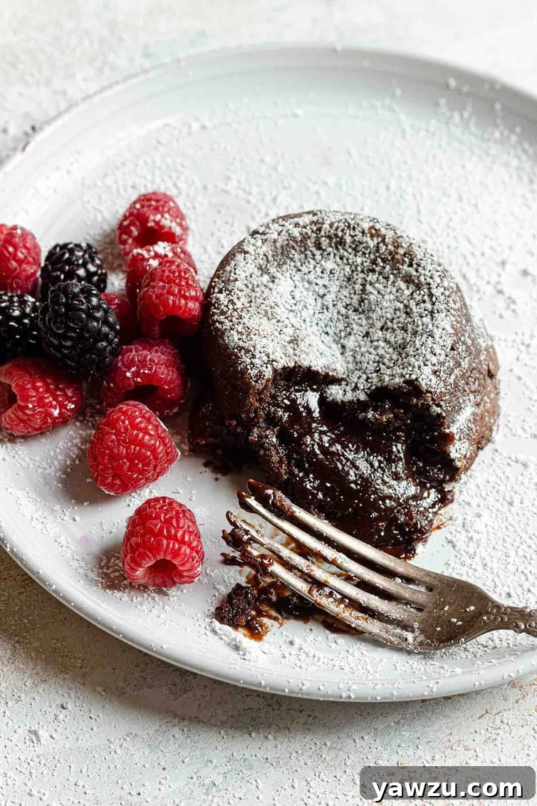 Chocolate lava cake on a white plate with a fork and raspberries.