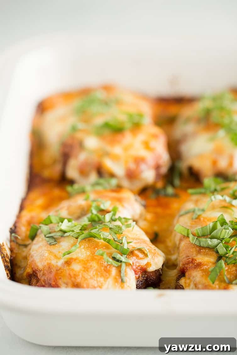 Four pieces of freshly baked chicken parmesan adorned with vibrant fresh basil leaves in a baking pan.