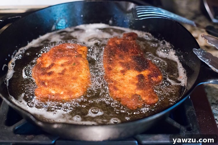 Chicken cutlets being pan-fried to a golden brown in a cast iron skillet, creating a perfect crust.