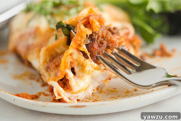 A fork lifts a generous bite of cheesy chicken parmesan, showcasing the melted cheese and crispy chicken.