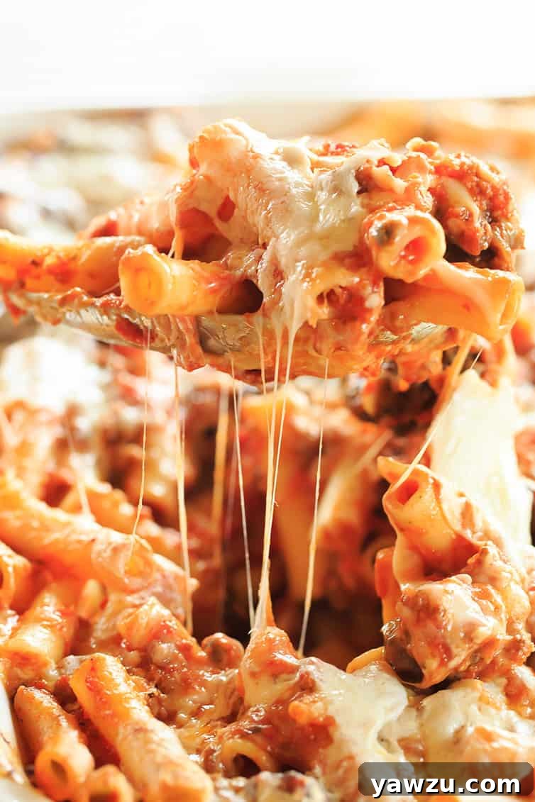 A generous serving of baked ziti being scooped from a large casserole dish, showcasing its gooey cheese and rich sauce.