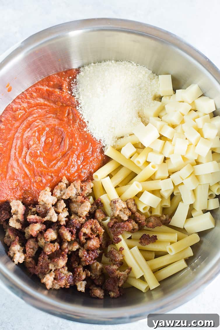 A large mixing bowl containing all the prepped ingredients for baked ziti – cooked ziti pasta, browned sausage, and sauce, before mixing.