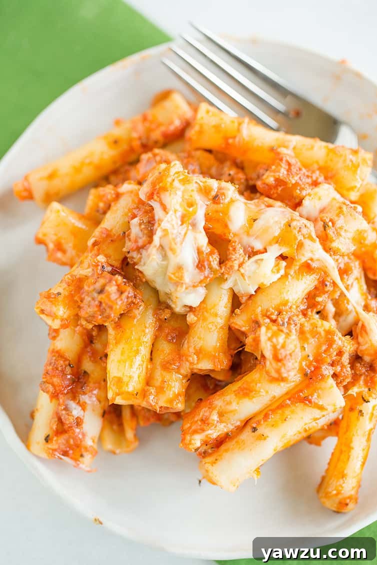 An inviting overhead view of a single serving of baked ziti on a white plate, showing melted cheese and rich sauce.