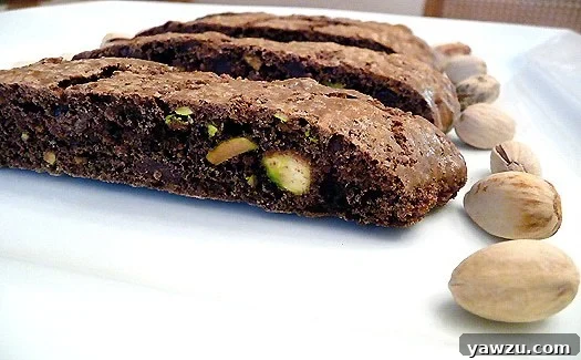 Pieces of chocolate pistachio biscotti on a white plate with pistachios.
