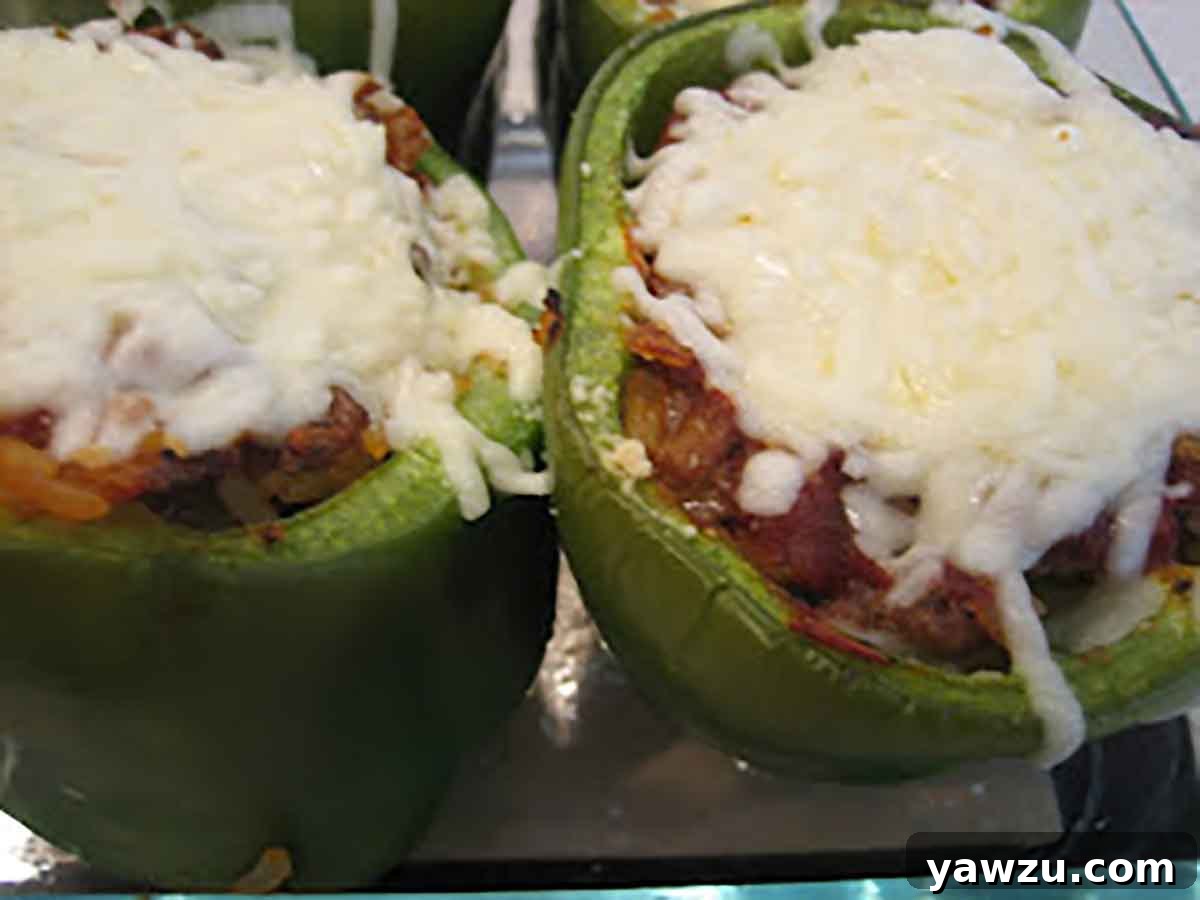 Two vibrant green bell peppers brimming with a savory meat and rice mixture, generously topped with melted, golden mozzarella cheese.