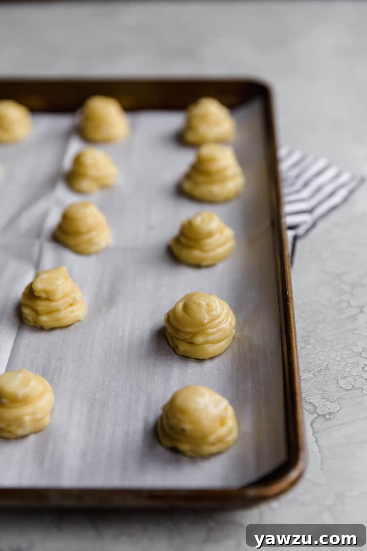 Neatly piped mounds of Gougères dough arranged on a baking sheet, ready for the oven.