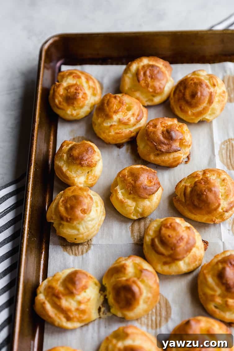 Golden-brown, perfectly puffed Gougères fresh out of the oven, still on the baking sheet.
