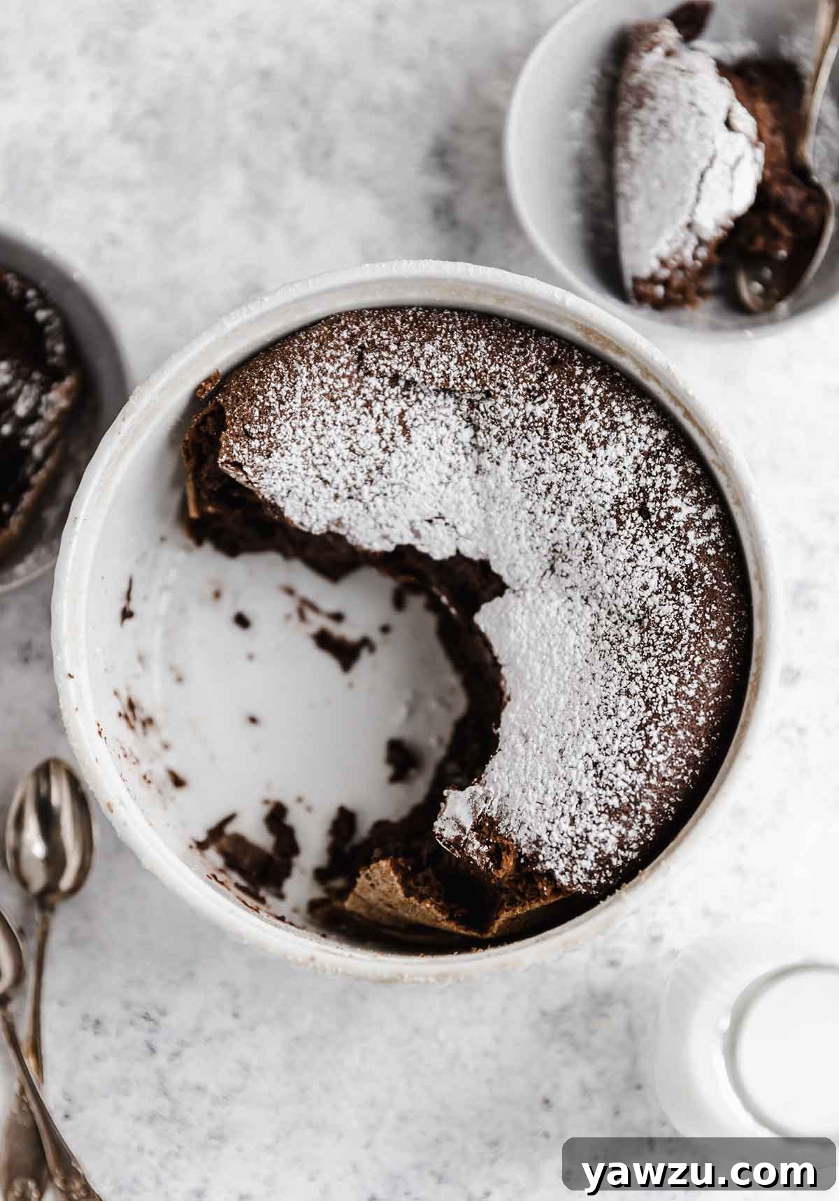Overhead photo of chocolate souffle with powdered sugar in a souffle dish, with half scooped out.