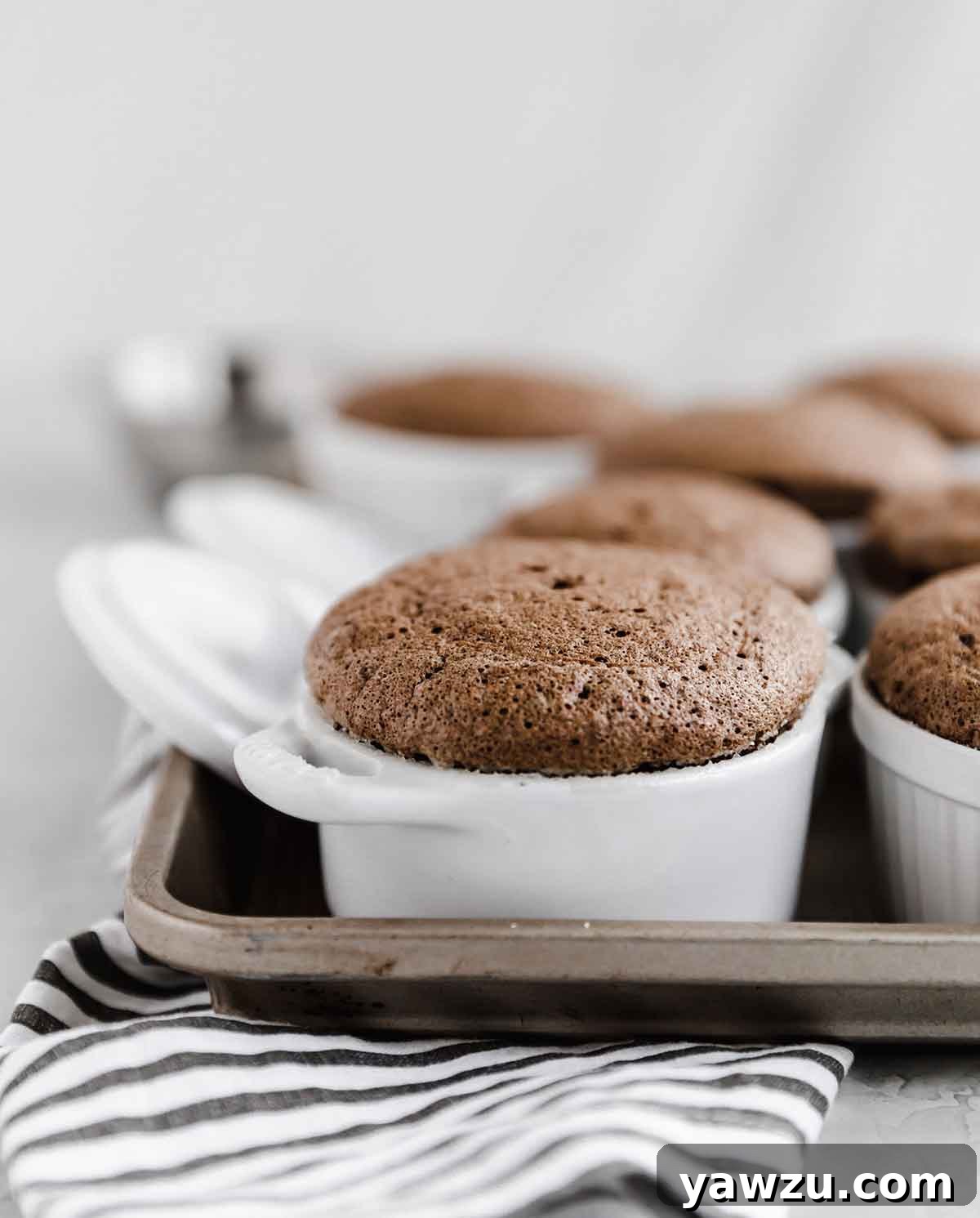 Individual chocolate souffles in small white ramekins sitting on a baking sheet.