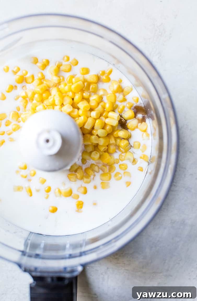 A food processor bowl containing fresh corn kernels and buttermilk, ready for blending.