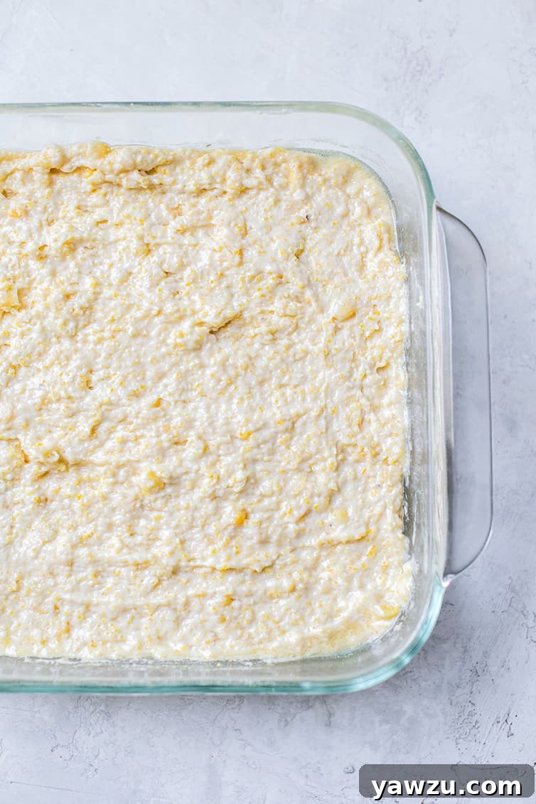 Cornbread batter evenly spread into a square baking pan, ready to be baked.