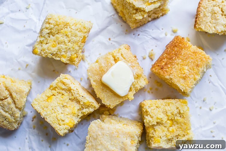 Two squares of cornbread on parchment paper, one with a melting pat of butter, emphasizing its moist texture.