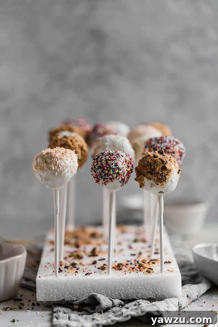 Vanilla cake pops standing upright in a styrofoam block, beautifully adorned with colorful sprinkles and cookie crumbs.